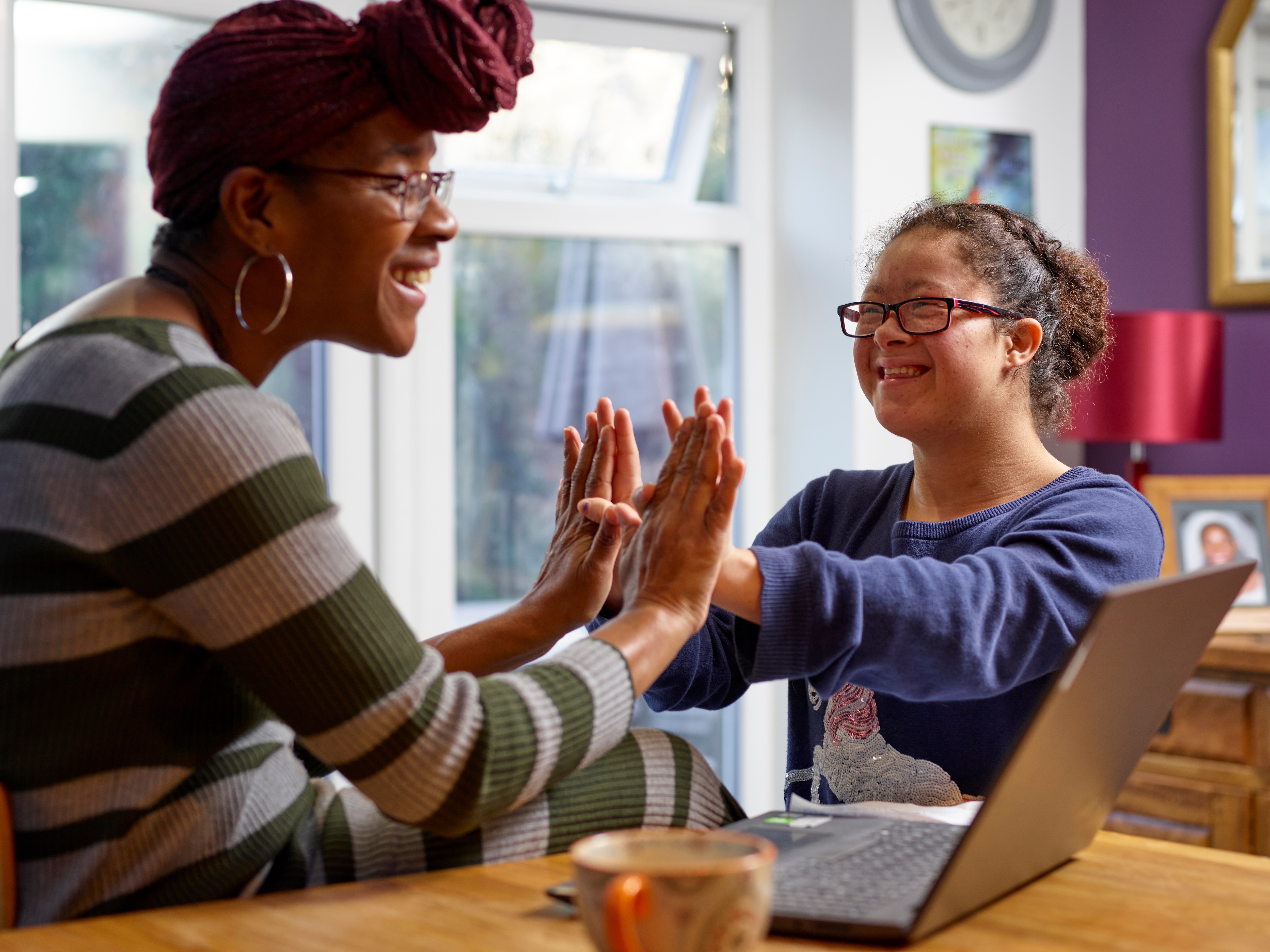 Woman with Down syndrome and her mom smiling and high-fiving in front of a laptop