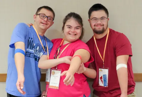 Tres participantes de HTP sonriendo y mostrando con orgullo sus vendajes tras la extracción de sangre