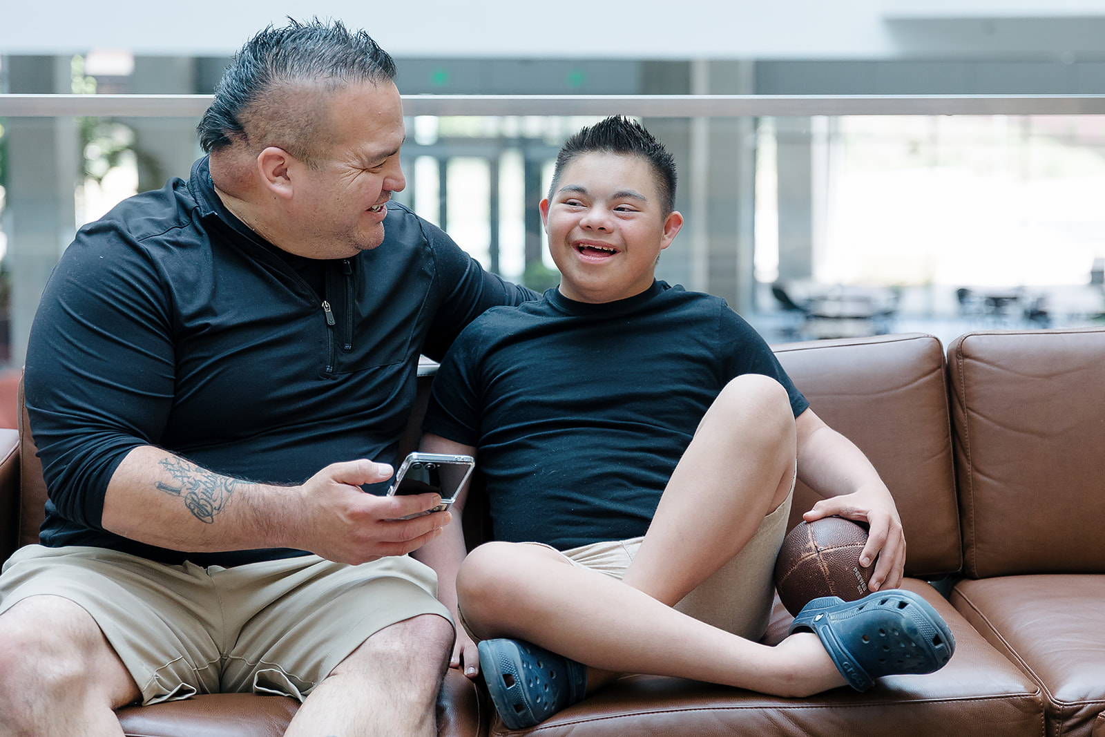 Boy with Down syndrome sitting next to his dad on a couch