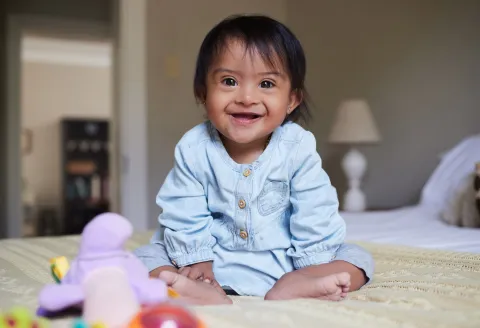 Bebé con síndrome de Down sentado en una cama