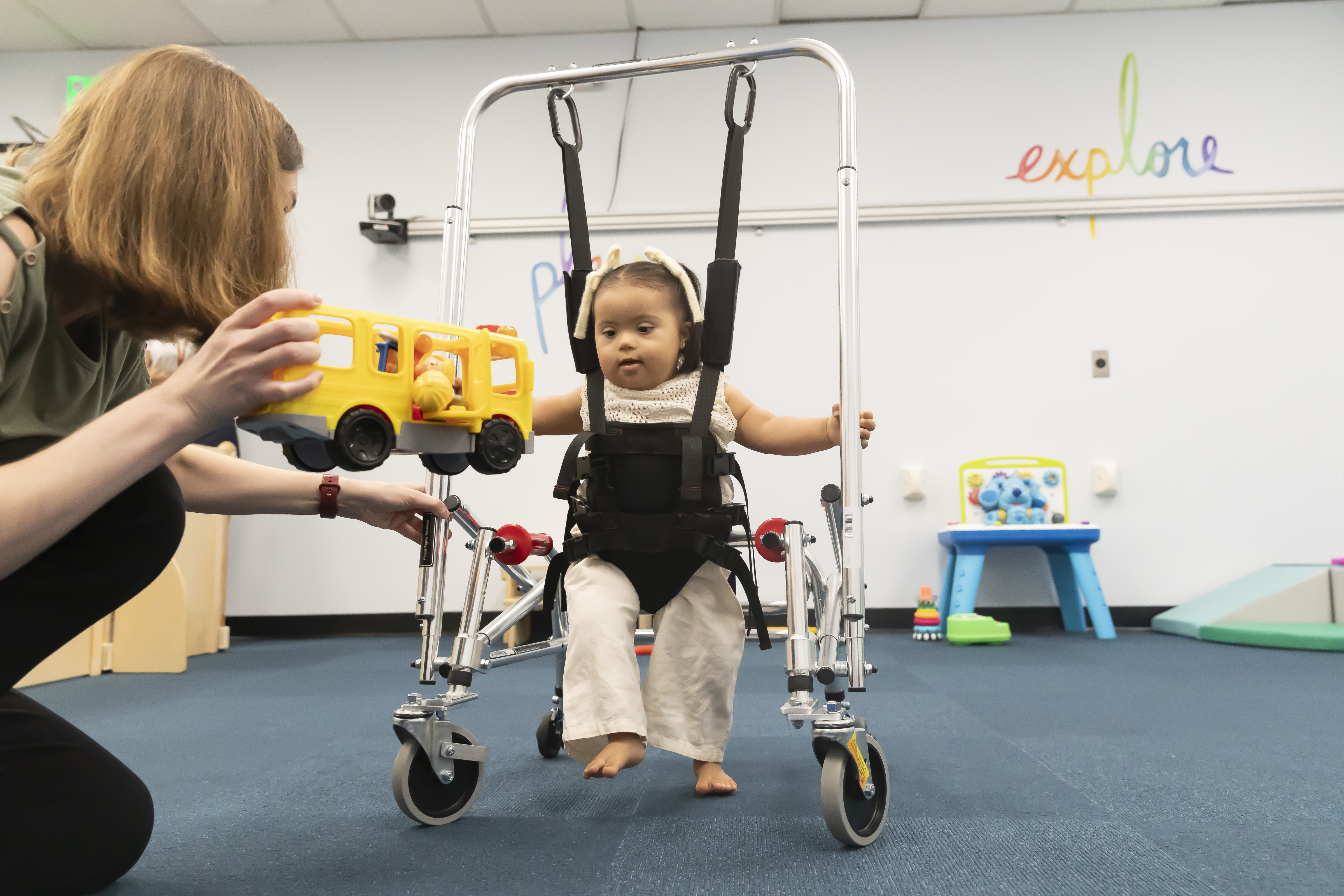 Girl with Down syndrome walking to toy bus being held by an adult with mobility device