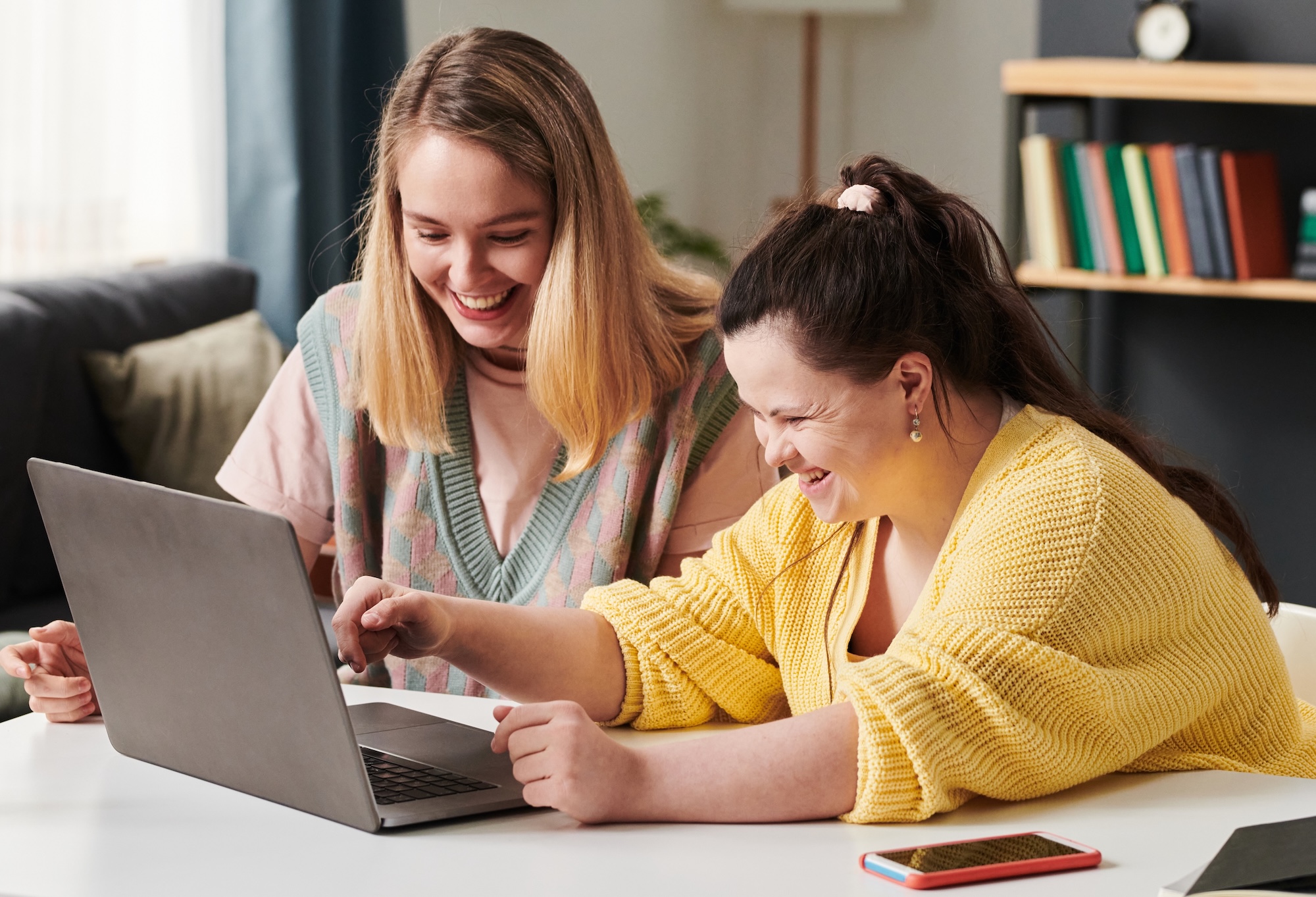 Woman smiling with a smiling woman with Down syndrome looking at a laptop