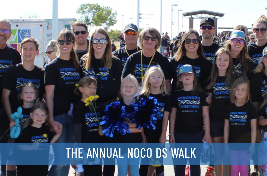 Un grupo de participantes de la Caminata Anual del Síndrome de Down del Norte de Colorado con el texto: LA CAMINATA ANUAL DEL SÍNDROME DE DOWN DEL NORTE DE COLORADO.