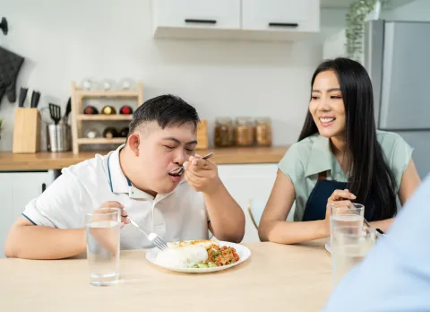 Young man with Down syndrome eating at a table with a family member