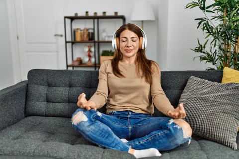 Woman sitting on a couch and meditating with headphones on