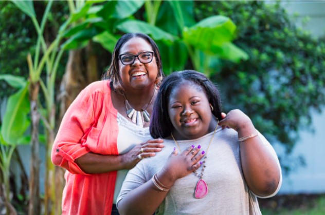 two women are embracing each other and smiling, one of the women has Down syndrome