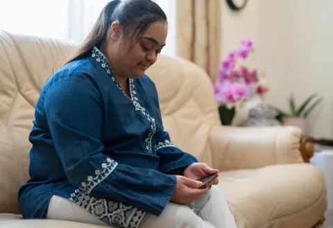 Woman with Down syndrome looking at a phone sitting on a couch