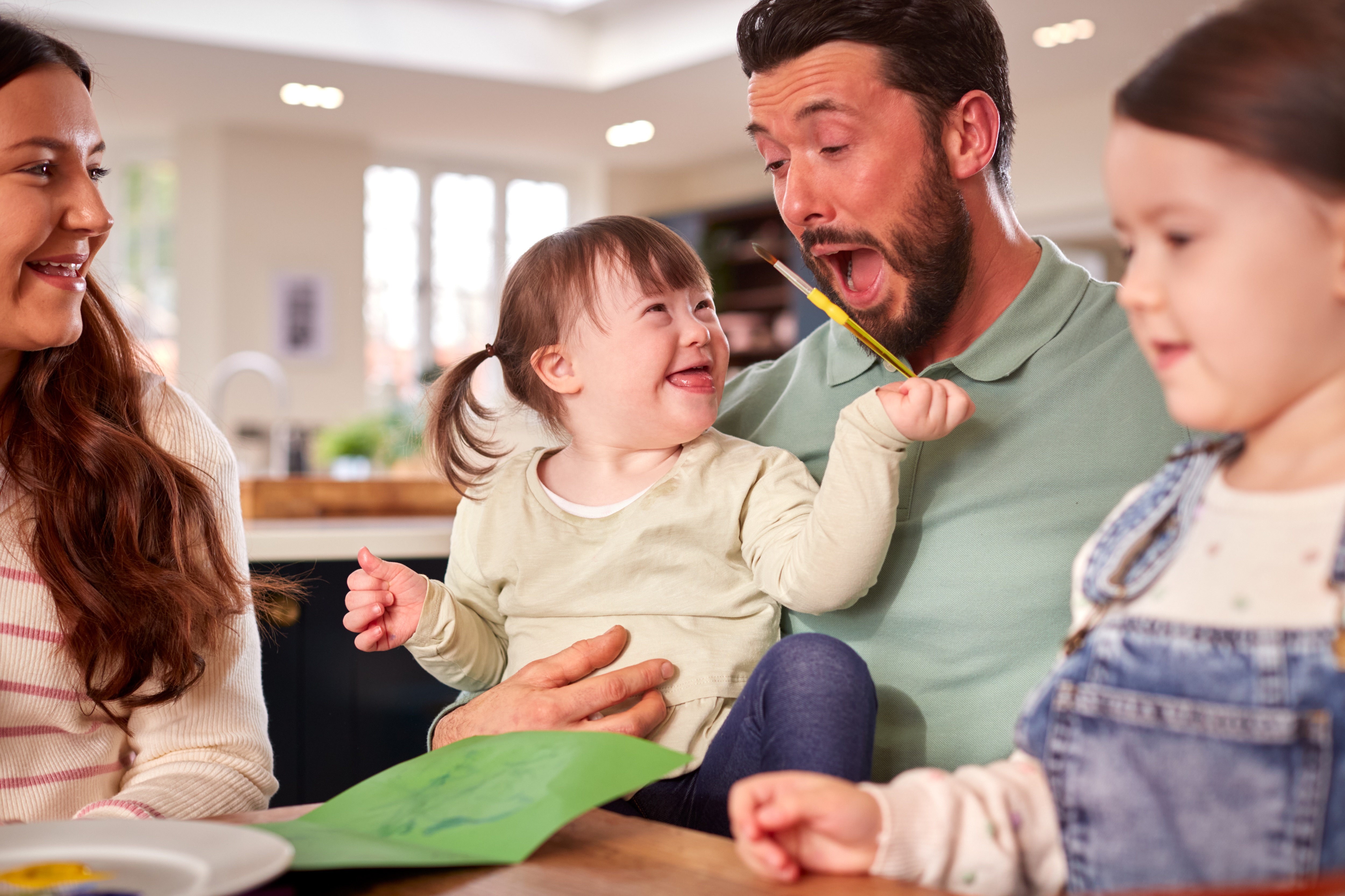 Child with Down syndrome smiling and sitting at the table with her family