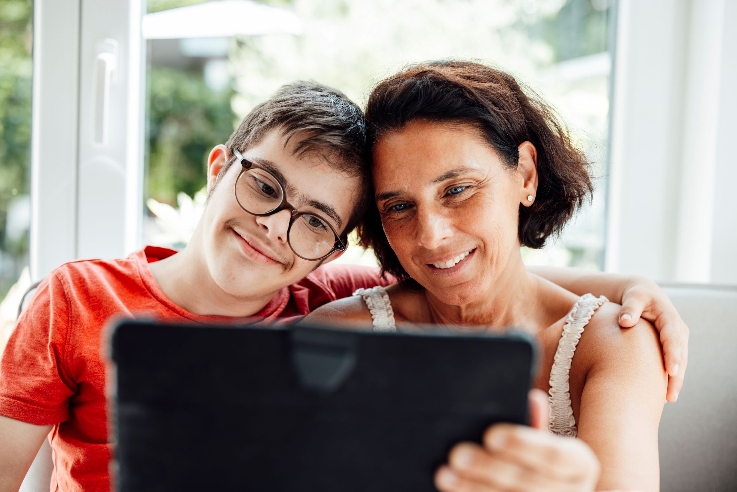 Mother and her teenage son with Down syndrome smiling and looking at a laptop